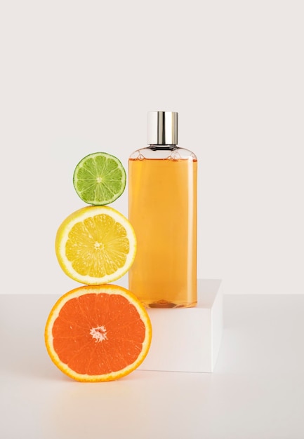 Un frasco de producto de cuidado cosmético en un podio blanco, los cítricos se encuentran uno al lado del otro