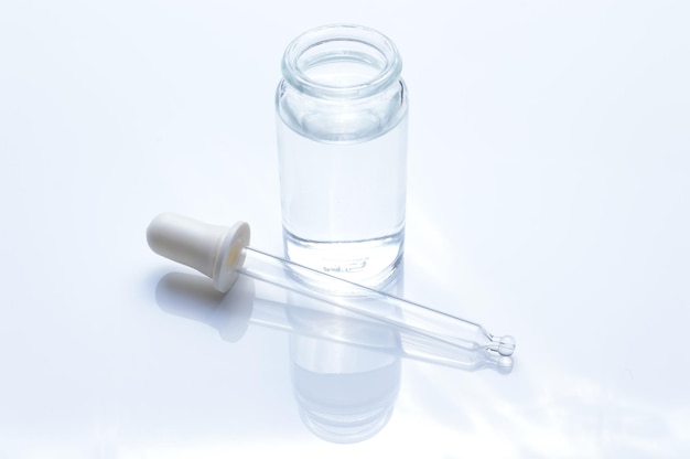 frasco transparente de vidro e uma pipeta cosmética com gotas líquidas em um fundo branco