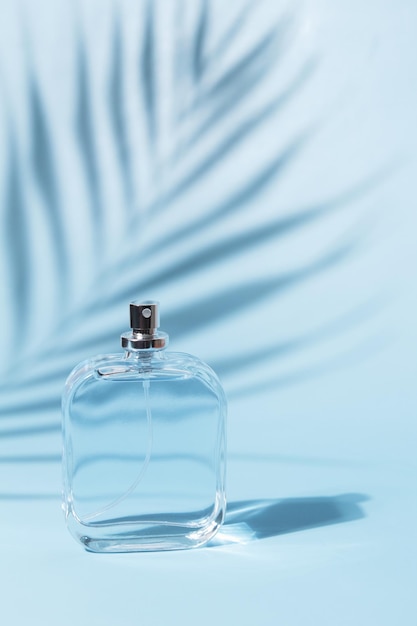 Frasco transparente de perfume sobre fondo azul Presentación de fragancia con luz de día con sombra de palma Esencia de mujer y hombre