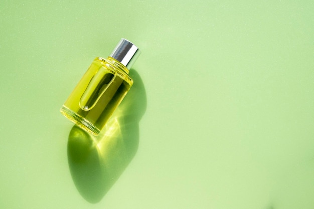 Frasco transparente de perfume sobre un fondo verde Luz natural y sombras Concepto de esencia de mujeres y hombres