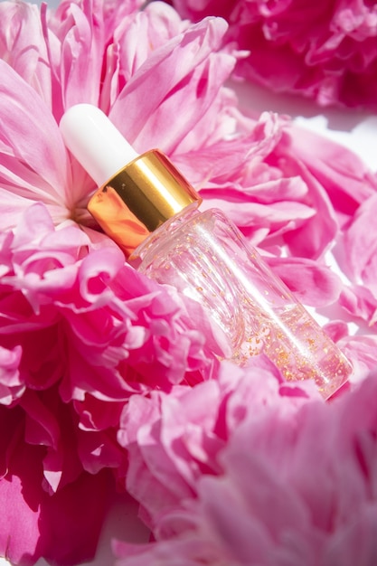 Frasco transparente con suero de belleza, ácido hialurónico, oro de 24 quilates y vitaminas con flores rosas. Mockup packaging, marca de diseño cosmético.