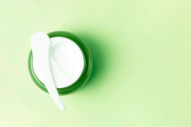 Frasco verde con crema blanca y espátula de plástico en el fondo, vista superior, espacio de copia