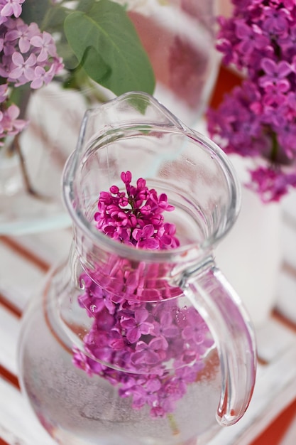 Frasco de vidrio de agua de flores lilas con rama fresca