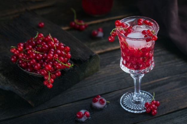 Un frasco de vidrio de bebida gaseosa de grosella roja sobre la mesa de madera oscura. Limonada, cóctel u otra bebida de desintoxicación saludable de verano. Bajo contenido de alcohol, bebidas no alcohólicas, concepto de dieta vegetariana o saludable.