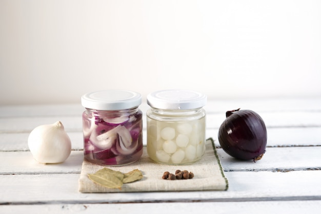 Frasco de vidrio de cebollas en escabeche sobre fondo de madera blanco