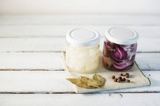 Frasco de vidrio de cebollas en escabeche sobre fondo de madera blanco