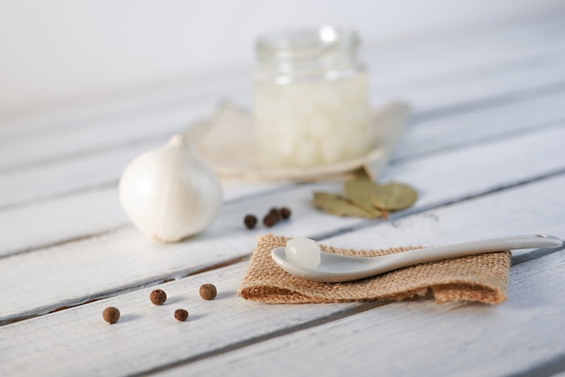 Foto frasco de vidrio de cebollas en escabeche sobre fondo de madera blanco