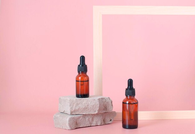 Frasco de vidrio cosmético con cuentagotas para cremas y sueros de aceites esenciales junto a la piedra El concepto de un salón de belleza y cosmética natural sobre un fondo rosa