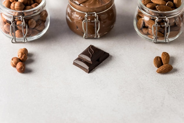 Frasco de vidrio con crema de nuez de chocolate y nueces crudas sobre un fondo concreto y trozos de chocolate
