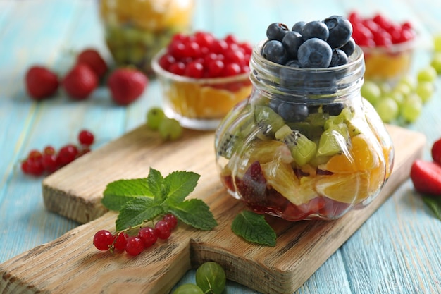 Frasco de vidrio con frutas frescas y bayas en tabla de cortar