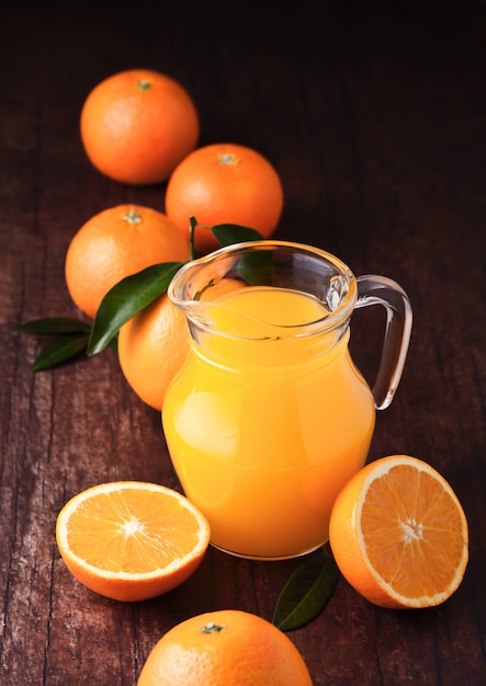 Frasco de vidrio de jugo de naranja fresco orgánico con naranjas crudas sobre fondo de madera oscura