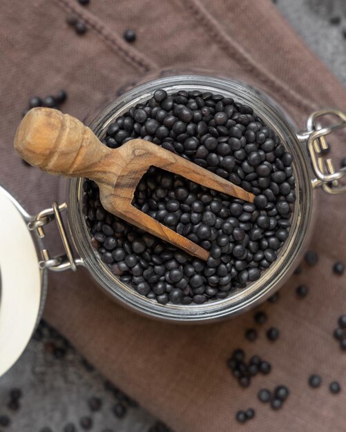 Frasco de vidrio de lentejas negras secas con una cuchara en la vista superior de la mesa gris dieta saludable de proteínas