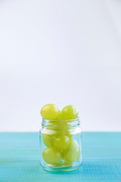 Frasco de vidrio lleno de uvas verdes caídas sobre una mesa