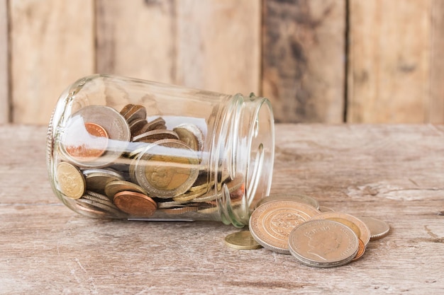 Frasco de vidrio con monedas en mesa de madera