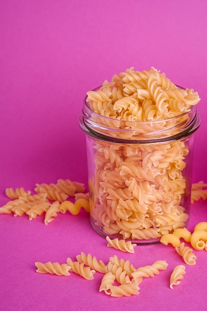 Foto un frasco de vidrio con pasta de trigo dorado crudo fusilli sobre fondo rosa mínimo, macro de vista de ángulo