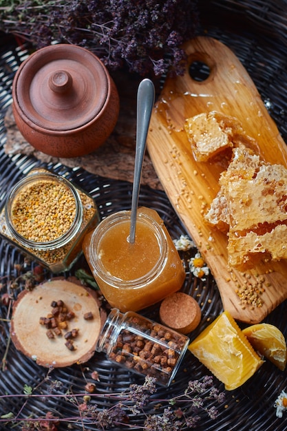 Foto un frasco de vidrio con polen, miel y propóleo sobre una tabla de madera se encuentra sobre una mesa de mimbre