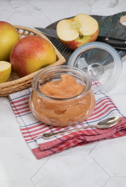 Frasco de vidrio con puré de manzana y manzanas frescas en un plato sobre un fondo claro con una servilleta a cuadros Orientación vertical