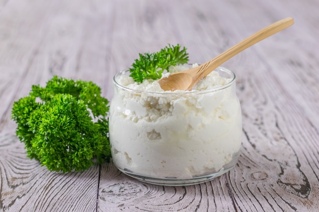 Frasco de vidrio con requesón fresco y hojas de perejil sobre una mesa de madera. El concepto de dieta saludable.