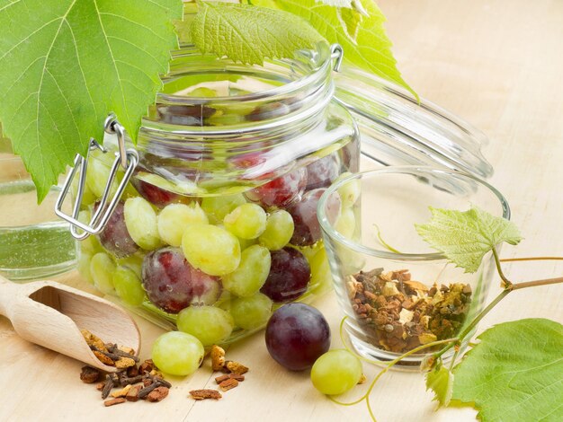 Frasco de vidrio con uvas enlatadas, hojas de uva y especias sobre mesa de madera