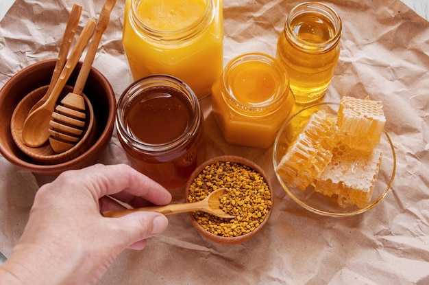 Frascos de abejas de miel natural de diferentes tipos de panal y polen en un tazón sobre la mesa Mano humana