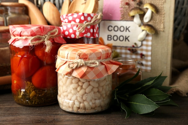 Frascos com especiarias de feijão de legumes em conserva e utensílios de cozinha em fundo de madeira