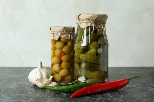 Frascos con conservas de pepinos y aceitunas en mesa ahumada negra