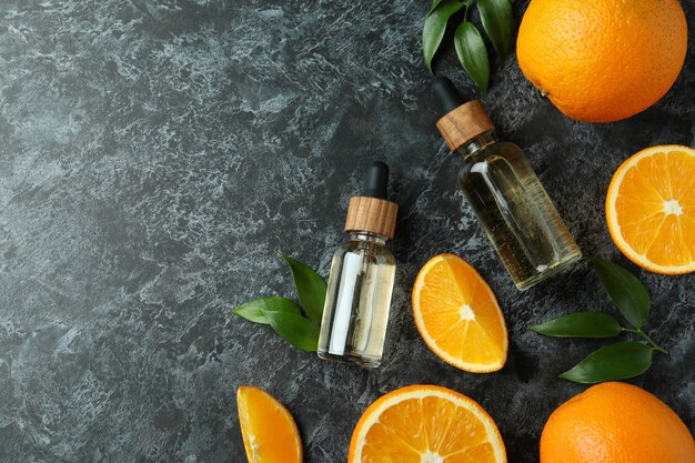 Foto frascos conta-gotas com óleo e laranjas na mesa preta esfumada