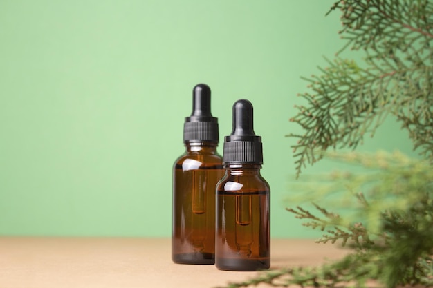 Frascos conta-gotas de vidro com óleo cosmético essencial ou soro em fundo verde com ramos de thuja Soro de óleo de ácido hialurônico com colágeno e peptídeos produto para cuidados com a pele