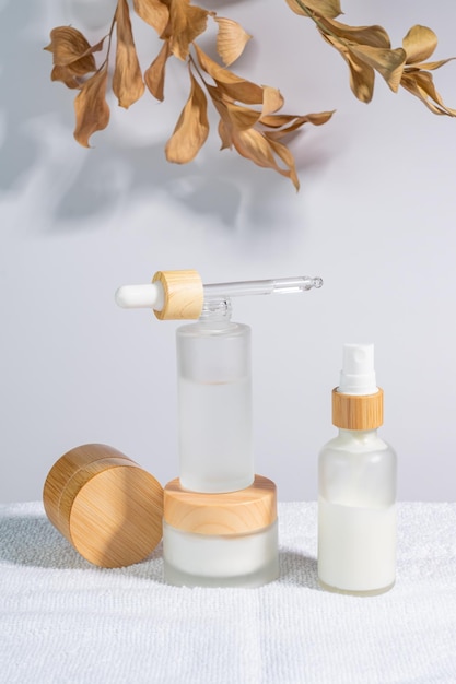 Frascos cosméticos de vidro fosco branco e frascos com tampas pamboo com folhas de árvore em fundo branco Rotina de cuidados com a pele definida para pele envelhecida