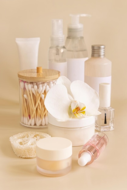 Frascos cosméticos naturales y accesorios para el cuidado de la piel con flor de orquídea blanca en beige de cerca