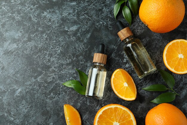 Frascos cuentagotas con aceite y naranjas sobre mesa ahumada negra