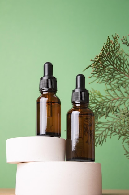 Frascos cuentagotas de vidrio con aceite cosmético esencial o suero en podio con ramas de thuja Cuidado cosmético de la piel facial y spa Concepto de tratamiento natural