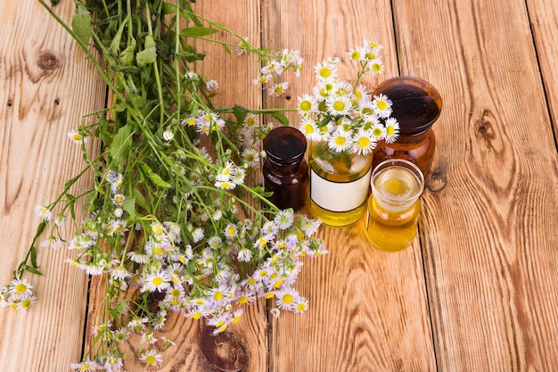 Frascos de conceito de fitoterapia com camomila e óleo na mesa de madeira