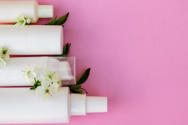 Frascos de cosméticos brancos, bomba de banho, sabonete artesanal, sal de banho, escova de massagem, esponja, cotonetes com flores de cerejeira em um fundo rosa. Conceito de cosméticos orgânicos naturais.