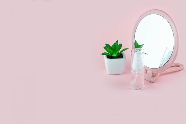 Frascos de cosméticos com soro, gel, creme para o rosto em um fundo rosa com uma flor e um espelho. Cosméticos para a pele, minimalismo