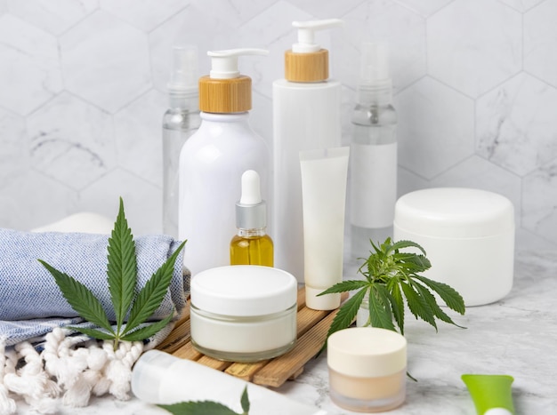 Frascos de cosméticos em branco, tubos e garrafas perto de folhas verdes de cannabis em bandeja de madeira no banheiro perto de outras garrafas fechar maquete Produtos de beleza orgânicos para a pele cosméticos naturais CBD