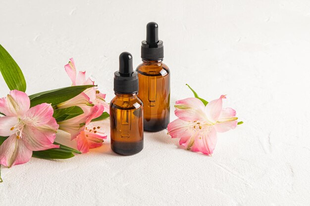 Frascos de cosméticos luxuosos com produtos de cuidados com a pele antienvelhecimento no fundo de cosméticos naturais de flores de astromeria rosa