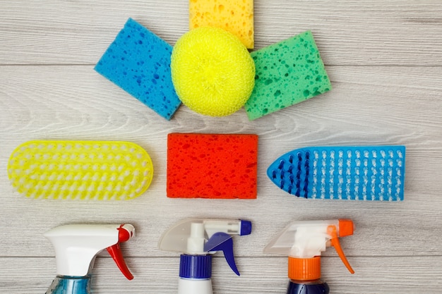 Frascos de detergente, esponjas sintéticas de cor para limpeza e escovas de pó sobre fundo cinza de madeira. Conjunto de ferramentas e equipamentos de limpeza