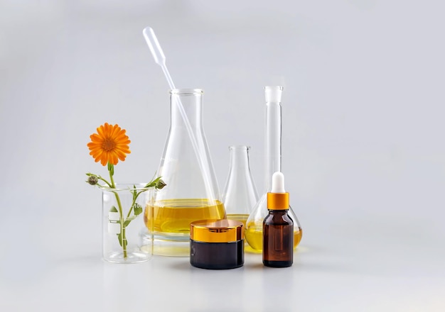 Frascos de laboratório de recipientes cosméticos e uma flor de calêndula em um fundo cinza