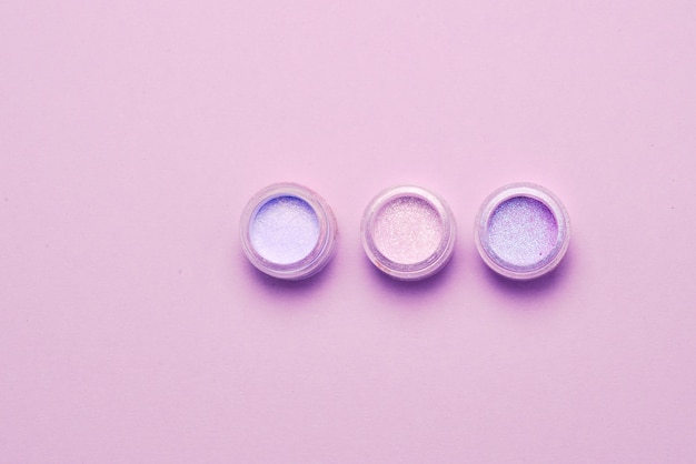 Frascos de maquiagem de cosméticos com sombras brilhantes e friáveis brilham Cores lilás verde rosa em fundo lilás Closeup espaço para texto ou design