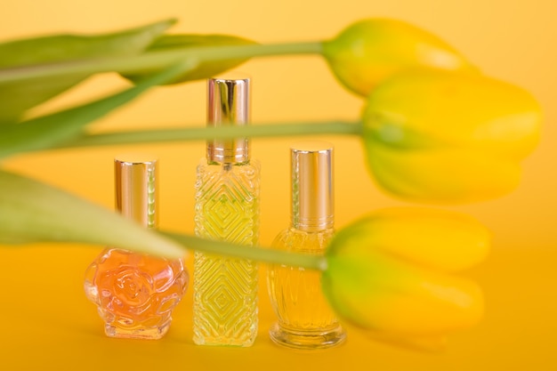 Frascos de perfume transparente diferente com buquê de tulipas em fundo amarelo