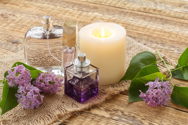 Foto frascos de perfume, uma vela acesa e flores lilás em um saco e velhas tábuas de madeira.