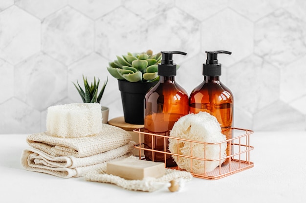 Frascos de sabonete e shampoo e toalhas de algodão com planta verde na mesa branca dentro de um fundo de banheiro.