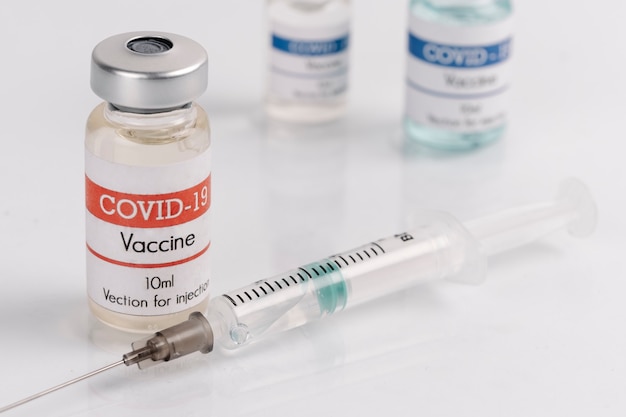 Frascos de vacina Covid-19 com seringa em uma superfície branca
