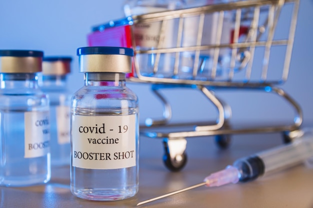 Frascos de vacina de reforço COVID-19 no carrinho de compras. Conceito de medicina e cuidados de saúde