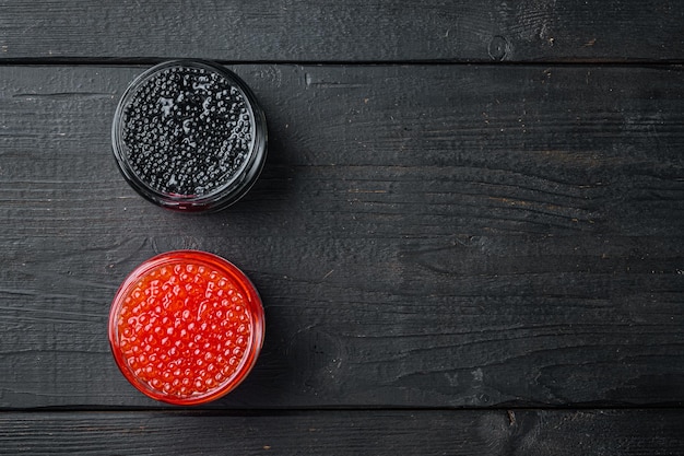 Frascos de vidro com caviar preto e vermelho, no fundo preto da mesa de madeira, vista de cima plana, com espaço de cópia para o texto