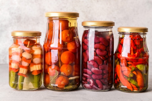 Frascos con diferentes verduras enlatadas y frijoles en mesa gris