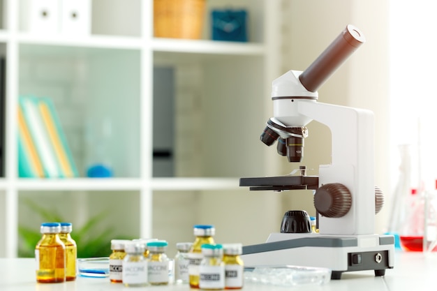 Frascos de frascos de vacunas y microscopio en la mesa en un laboratorio científico