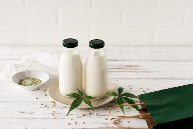 Foto frascos con gluten vegano a base de hierbas de cannabis y leche sin lactosa y hojas de cannabis en la mesa de madera.