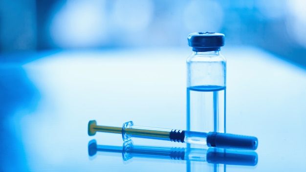 Frascos de medicamentos y jeringas en una mesa de cristal azul con ventana. Jeringa de insulina y aguja para diabetes. suministros para diabéticos
